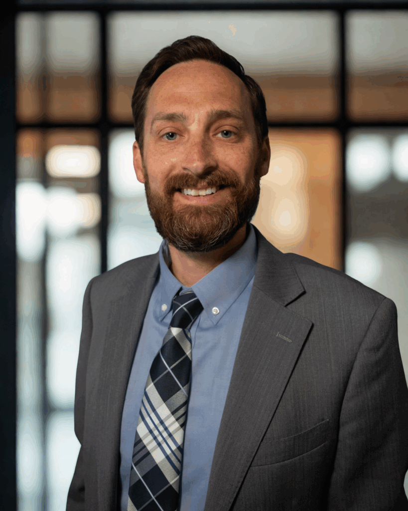 Cyrus Nate Lawyer headshot with smile, grey suit, plaid tie. Carr & Carr Injury Attorneys